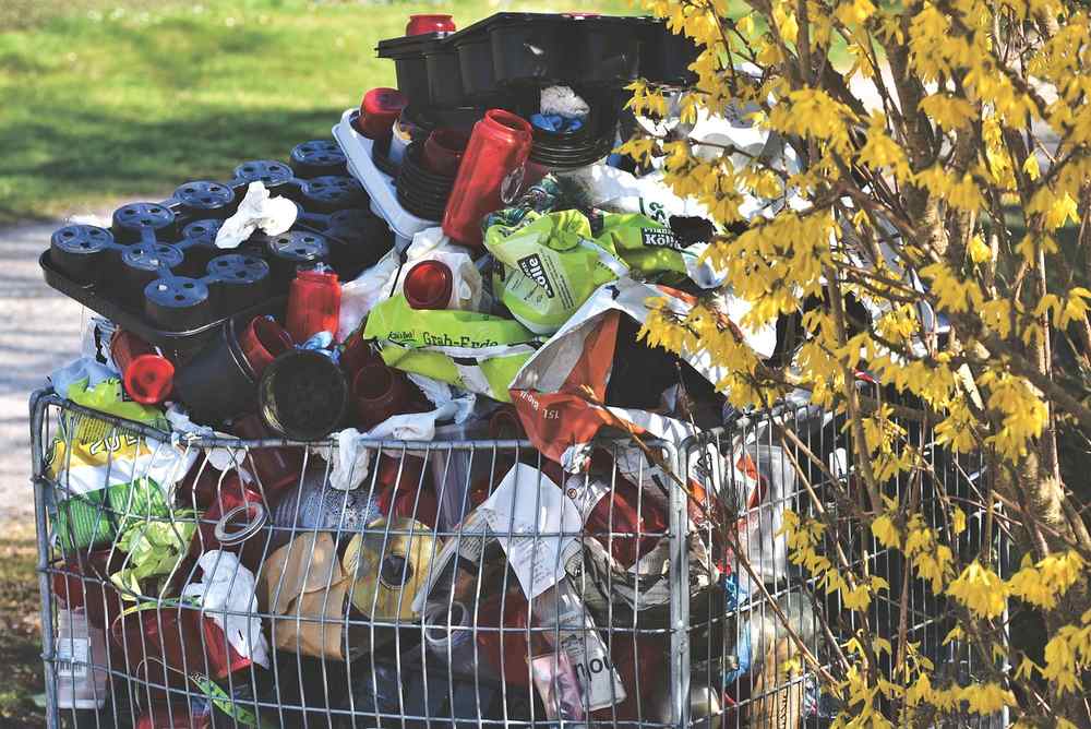 Cage métallique remplie de déchets variés près d'un arbre en fleurs