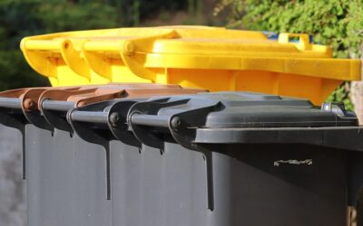 Trois poubelles extérieures, couvercles jaunes, bruns et gris, dans un décor vert