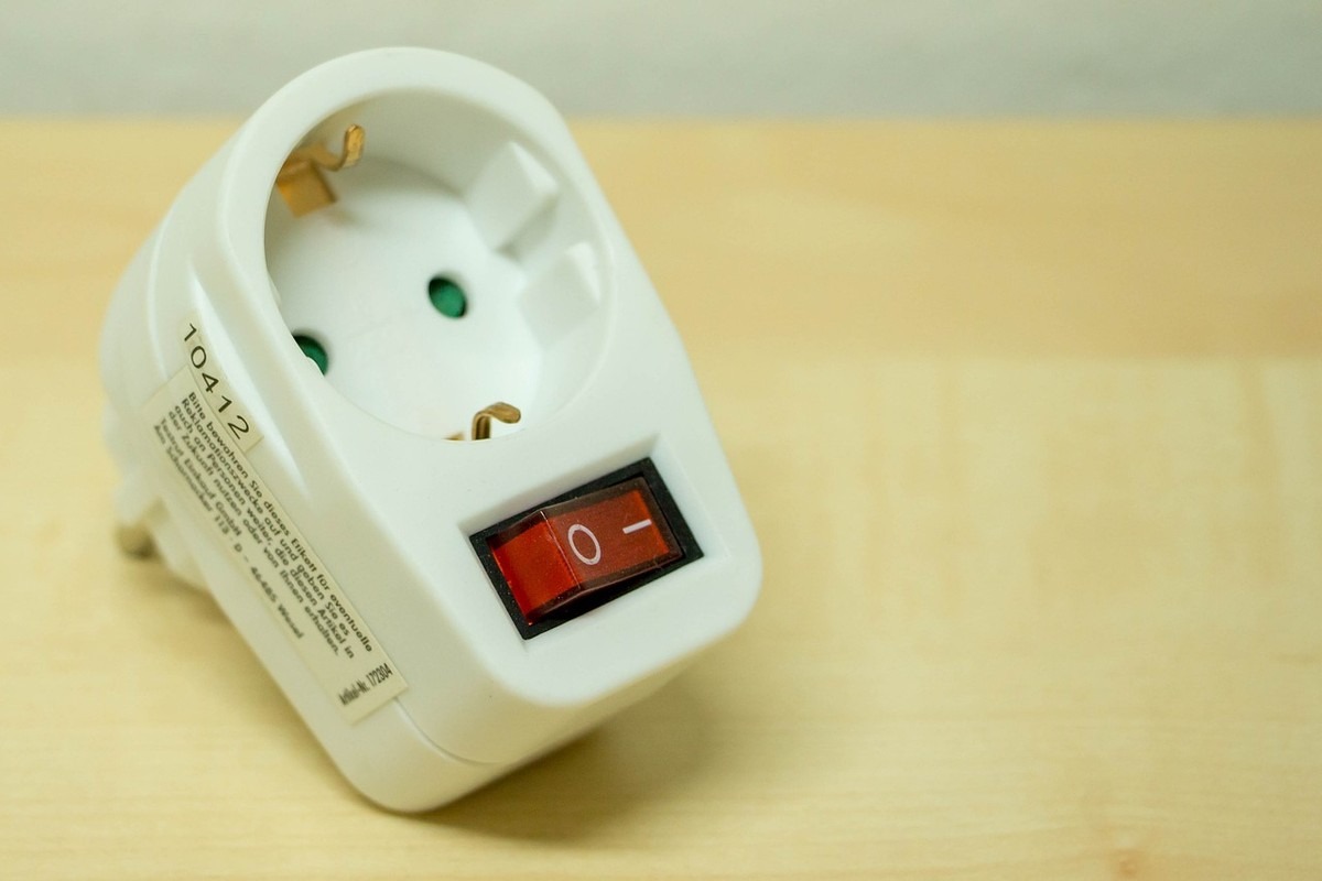 Adaptateur électrique blanc avec interrupteur rouge sur plan de bois Adaptateur électrique blanc avec interrupteur rouge sur plan de bois