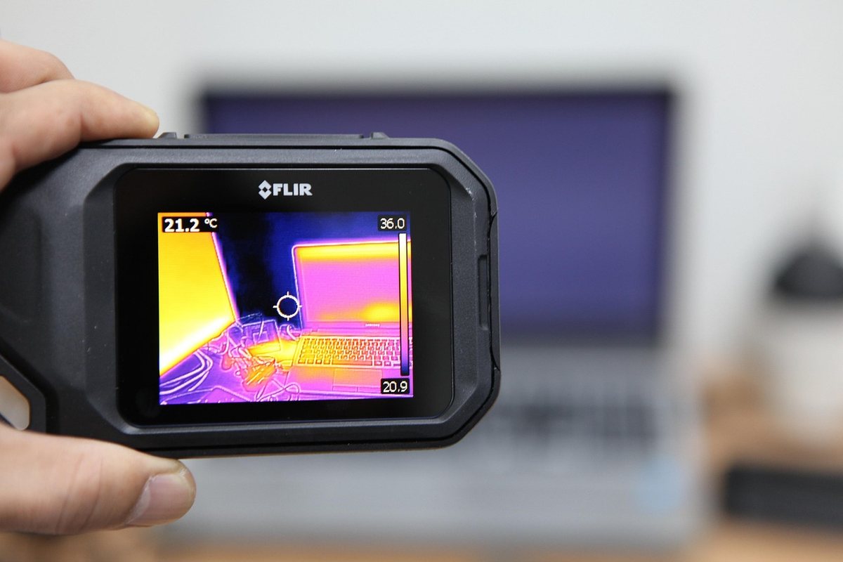 Une main tient un appareil thermique FLIR affichant la carte de chaleur d'un ordinateur