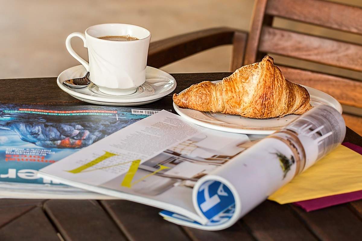 Café, croissant, magazines et serviettes sur une table en bois Café, croissant, magazines et serviettes sur une table en bois