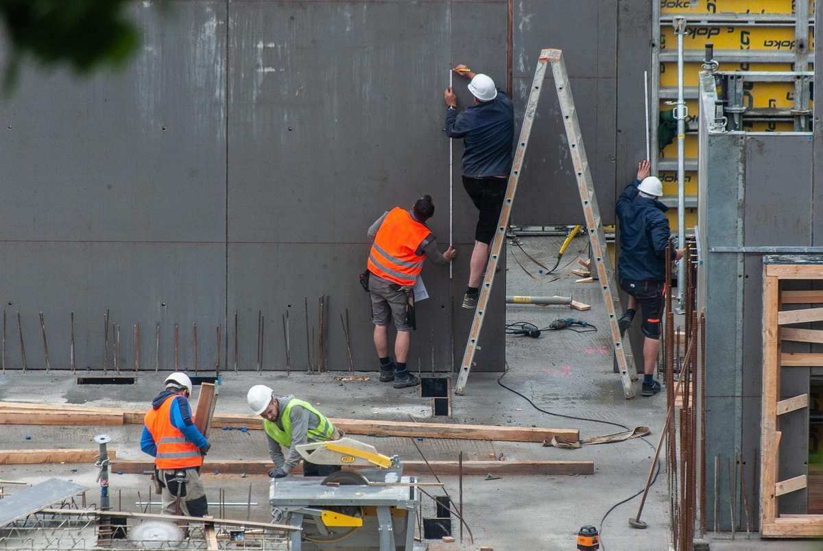 Travailleurs en casque posent panneaux sur mur, utilisent échelles Travailleurs en casque posent panneaux sur mur, utilisent échelles
